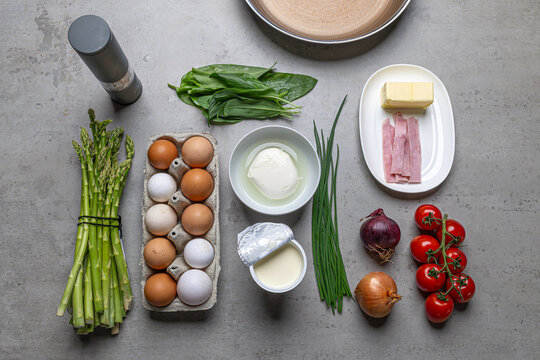 Cooking an italian frittata with mozarella, asparagus, eggs, onions, tomatoes and fresh herbs in spring time at home in the kitchen