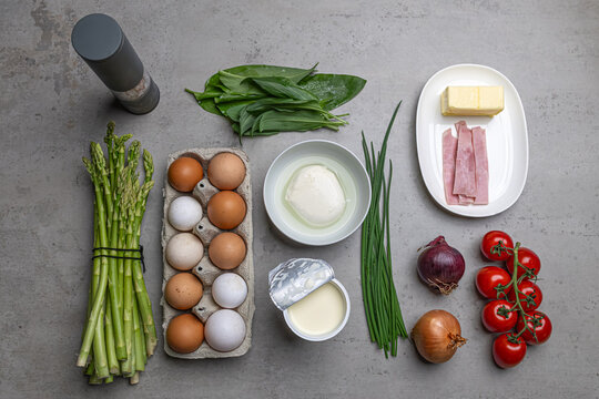 Cooking an italian frittata with mozarella, asparagus, eggs, onions, tomatoes and fresh herbs in spring time at home in the kitchen
