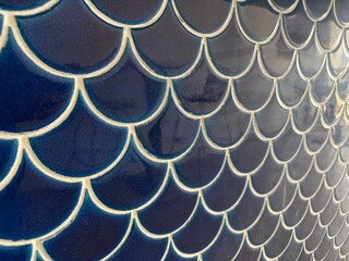 Deep blue ceramic tiles forming an intricate mermaid fish scale pattern. Creating a textured wall surface with contrasting grout lines © Tetyana
