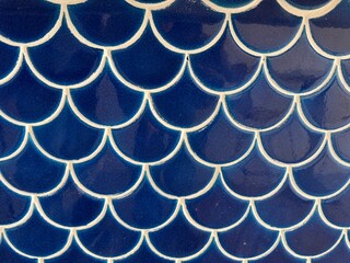 Dark blue ceramic tiles in a fish scale pattern creating a textured background, representing elegant aquatic design, ocean aesthetic, and decorative wall surfaces © Tetyana