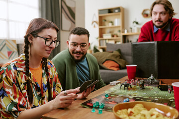 Fototapeta premium Young adult friends playing tabletop role playing game, reading cards and planning moves at home
