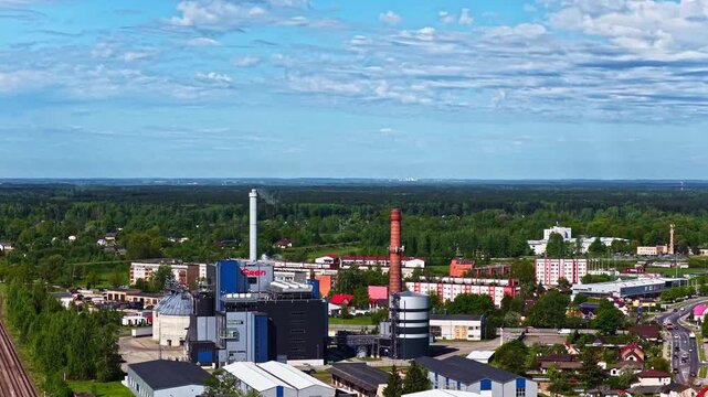 Panoramic drone shot of an industrial heating plant surrounded by green forests and city outskirts.