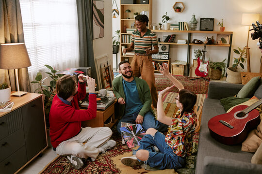 Multiethnic young adults socializing around vinyl records in living room, dancing and sharing music