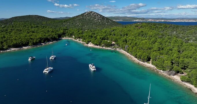 Aerial view of  turquoise bay with anchored sailboats and a yacht along a forested coastline near Zadar, Croatia.