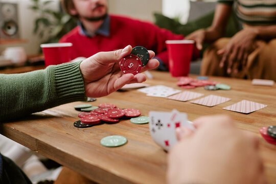 Close up of young adults playing poker, holding cards and betting chips during home gathering
