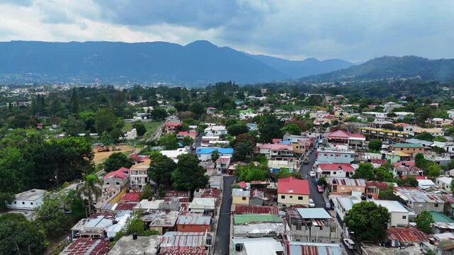Dense tropical Jarabacoa town nestled between mountains under cloudy sky from above, La Vega, Dominican Republic