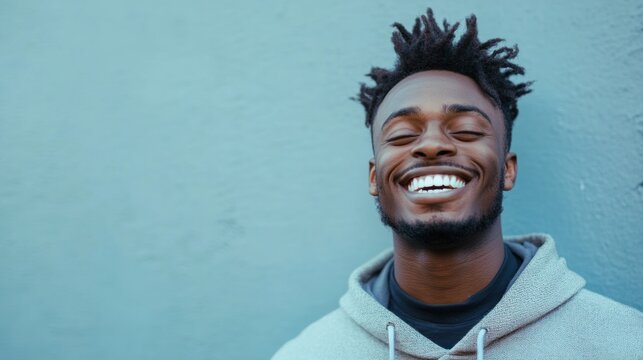 Joyful young man smiles against a light-blue wall, expressing happiness and contentment