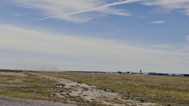 A powerful C-17 Globemaster III taking off from a distant airport runway. The aircraft ascends against a backdrop of a clear blue sky, kicking up dust as it begins its journey.