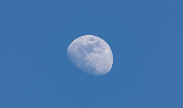 Half moon visible in blue daytime sky with clear background