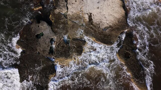 Top down drone view of powerful Caspian Sea surf at 43km Mangystau, Aktau. Aerial footage of massive coastal boulders with white waves crashing against them on a sunny summer day. Abstract beauty 