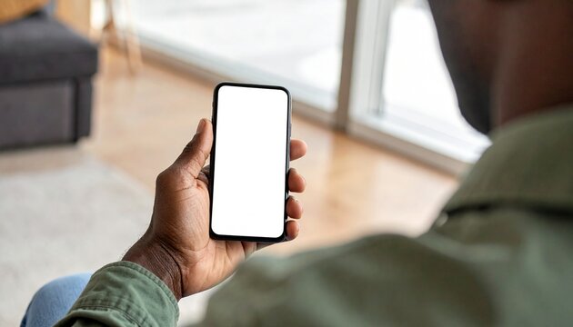 A person holds a smartphone with a blank screen, seen from over the shoulder, indoors