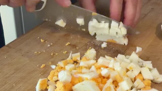Chef meticulously dicing a hard boiled egg with a knife on a wooden cutting board for a healthy and nutritious meal, a protein rich ingredient for a homemade salad