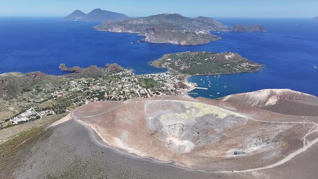 Drone flying circular path above Vulcano volcano showing crater and Lipari island in distance.