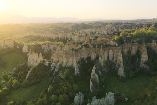Aerial view of Le Balze del Valdarno geological formations with clay cliffs and lush green vegetation under golden hour light in Botriolo, Toscana, Italy.