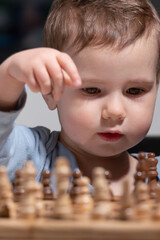 Naklejka premium Toddler interacting with wooden chess set, symbol of early intellectual development.