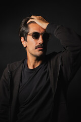Fototapeta premium Stylish man in sunglasses poses thoughtfully in studio light