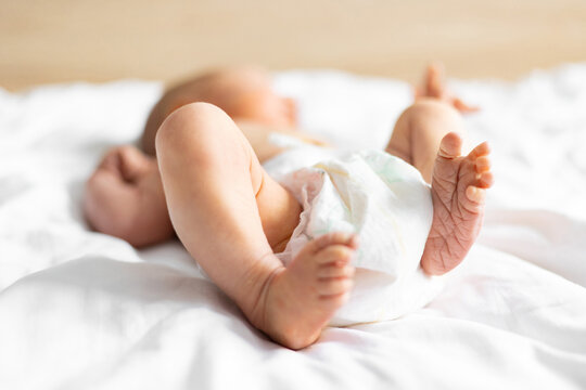 Close-up of a Caucasian newborn baby's tiny feet and legs, wearing a diaper and lying on soft white sheets