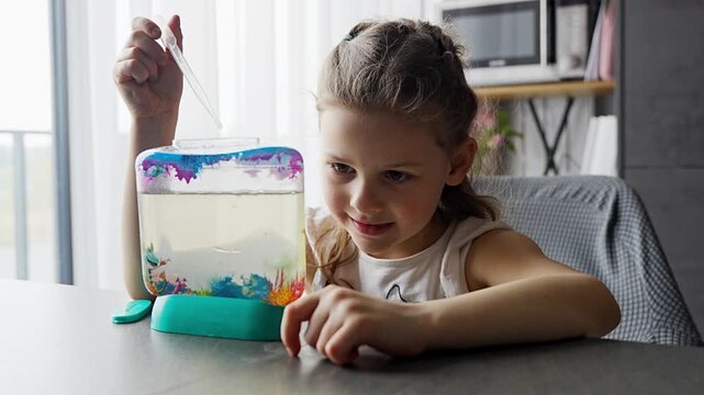 Little girl creating air bubbles in aquarium with artemia using pipette. Simple home science experiment exploring oxygenation and aquatic micro life concept.