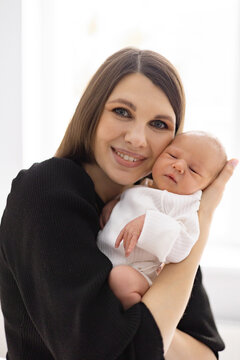 A smiling mother lovingly cradles her newborn infant in her arms, capturing a tender moment of maternal connection and family bonding