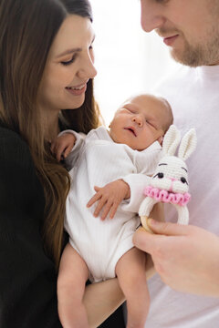 A loving family shares a tender moment with their newborn baby, holding a cute bunny rattle