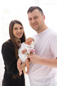 A smiling mother and father hold their adorable newborn baby, who clutches a cute bunny toy