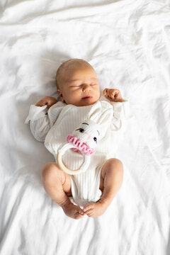 A peaceful Caucasian newborn baby sleeps soundly on a white sheet, clutching a cute bunny rattle