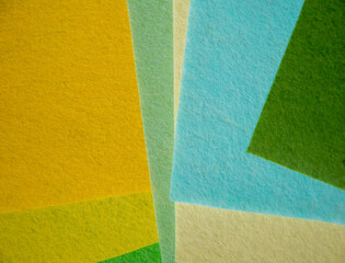 Fototapeta premium Multiple colorful felt fabric sheets in green, yellow, golden amber, mint, cream, sky blue and forest green overlapping in geometric layered composition — vibrant nature-inspired textile color palette