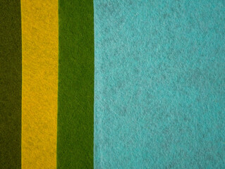 Fototapeta premium Close-up flat lay of colorful felt fabric sheets arranged in bold vertical color blocks — light cream/beige, dark olive green, bright yellow, grass green, and turquoise/sky blue. 