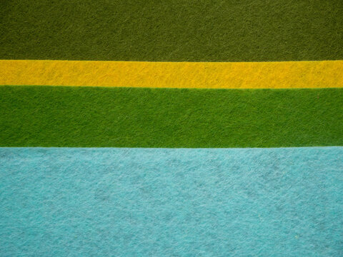 Close-up flat lay of colorful felt fabric sheets arranged in bold color blocks &mdash; light cream beige, dark olive green, bright yellow, grass green, and turquoise sky blue. Soft fibrous felt  texture.