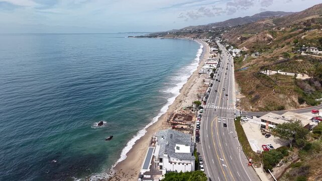 Cinematic 4K 10-bit aerial drone footage captured hovering above the shoreline in Malibu, featuring a steady bird&rsquo;s-eye view of ocean waves rolling onto the sandy beach.