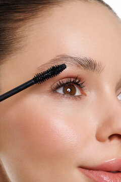 Young woman applying mascara on white background