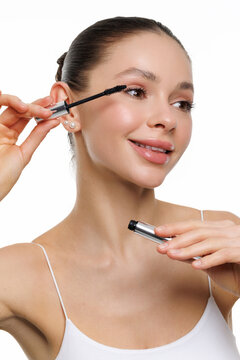 Beautiful young woman applying mascara on grey background