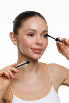 Young woman applying mascara on white background