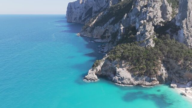Stunning drone shot of the iconic Cala Goloritze beach featuring crystal clear turquoise water and dramatic limestone rock formations in Sardinia, Italy.