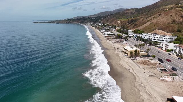Cinematic 4K 10-bit aerial drone footage captured above the shoreline in Malibu, featuring a smooth forward dolly movement over the beach and ocean waves.