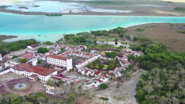 Drone aerial shot of the abandoned ghost hotel beside the Lagoon of Seven Colors in Bacalar, Mexico. Unique ruins surrounded by turquoise water, tropical nature, and iconic travel scenery.