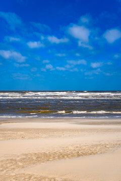 North Sea beach on the East Frisian island of Spiekeroog (Germany) on a stormy day with strong surf, sunshine, and blue skies. The stromy wind blows the fine sand near the shore out into the sea. 