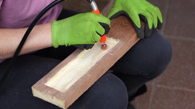 Working with an engraver. A woman cuts and processes wood; a woman creates handmade wood crafts using an engraver. Handcrafted woodwork in progress.
