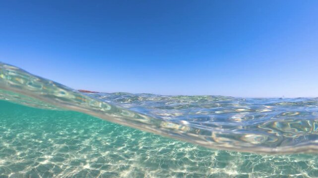 Slow motion split underwater view of La Pelosa beach showing clear turquoise water above and below the surface