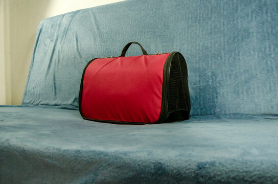 Red and black pet carrier with mesh ventilation on blue couch. Portable animal transport solution for veterinary visits, travel, and safe commuting with cats or dogs