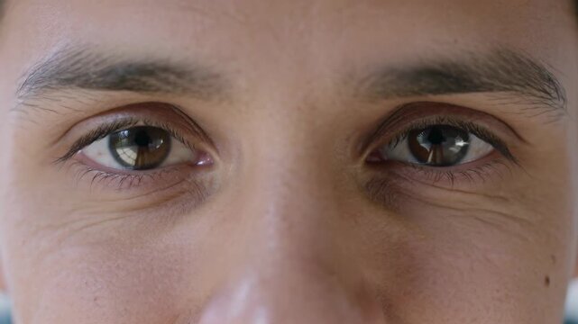 Holding steady eye contact, man making slow blinks, narrowing lids in studio at light reflection
