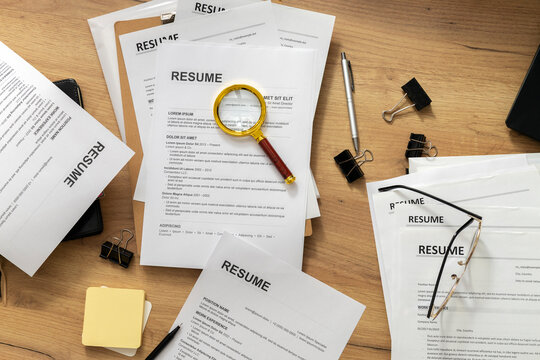 Top view of magnifying glass over resume symbolizing detailed background check and careful candidate screening by HR specialist during recruitment process