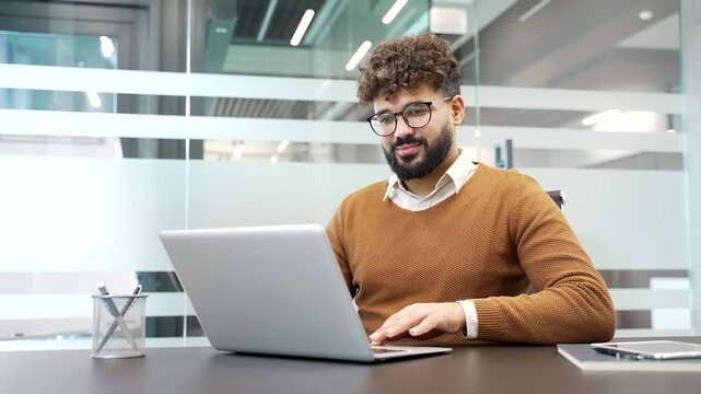 Businessman working on a laptop sitting at workplace in modern business office. Smiling worker typing on computer, engaged with a task, banking, texting client, chatting online or busy with a project