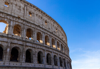 Fototapeta premium Famous Coliseum in Rome. Colosseum, or Coliseum. Part of the wall of an antique stone structure with arches. Italy, Europe. Famous touristic place in the world, Europe. Beautiful blue sky background.