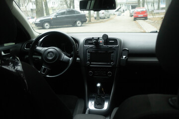 Obraz premium View from parked car showing dashboard and street lined with trees and buildings in the background during the day