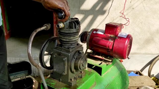 Close-up view of a technician&rsquo;s hands repairing and adjusting an air compressor pump connected to an electric motor. It highlights industrial maintenance, mechanical work, and repair in a workshop.