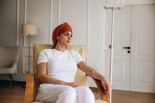 Female patient undergoing chemotherapy treatment in a hospital setting, wearing a headscarf and seated in a comfortable chair with an IV drip nearby