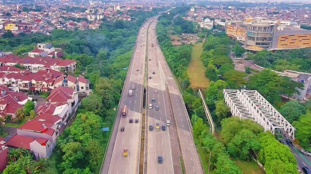 Aerial Drone View of Urban Toll Road Traffic in Indonesia with Residential Area and Green Landscape