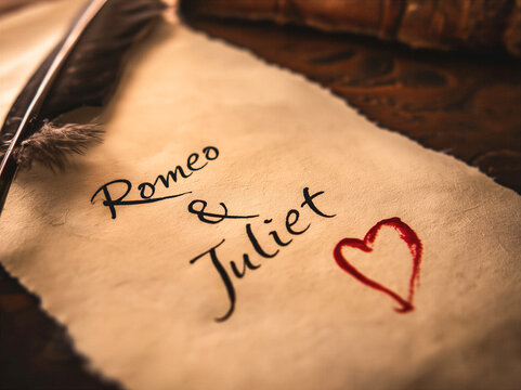 the words written in a quill Romeo and Juliet and a drawn red heart, a feather quill lays to the side. authentic scene