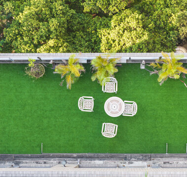Aerial view of a rooftop terrace with white garden furniture on green artificial turf overlooking lush trees in Taiwan.